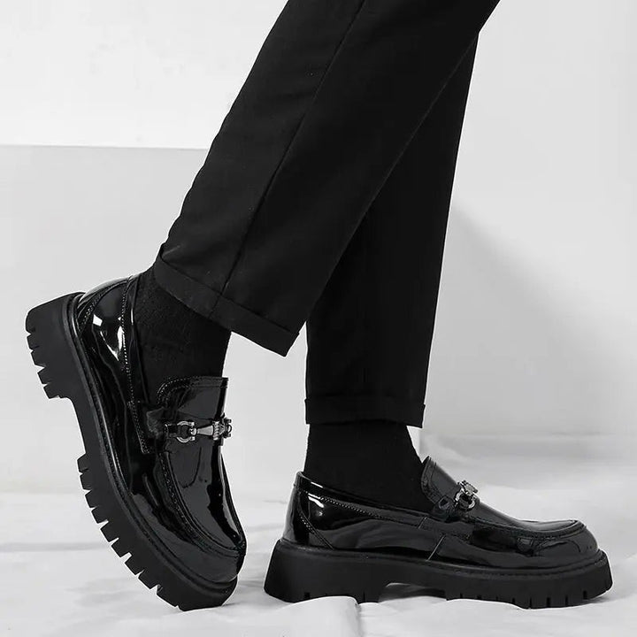 Black patent leather loafers worn with cuffed trousers, chunky sole in profile