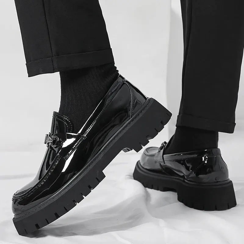 Close-up of black patent loafer with metal trim, black socks and rolled hem