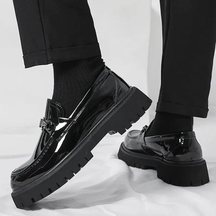 Close-up of black patent loafer with metal trim, black socks and rolled hem