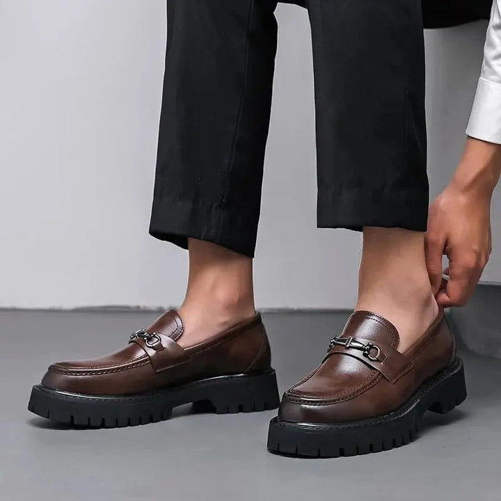 Close-up of brown leather loafers worn with black trousers, metal snaffle trim