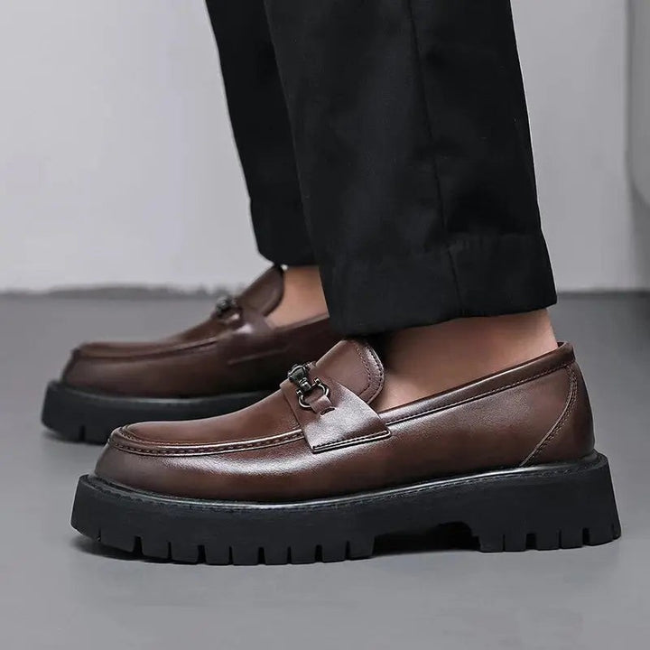 Side view of brown leather loafers with buckle trim, model adjusting trouser hem