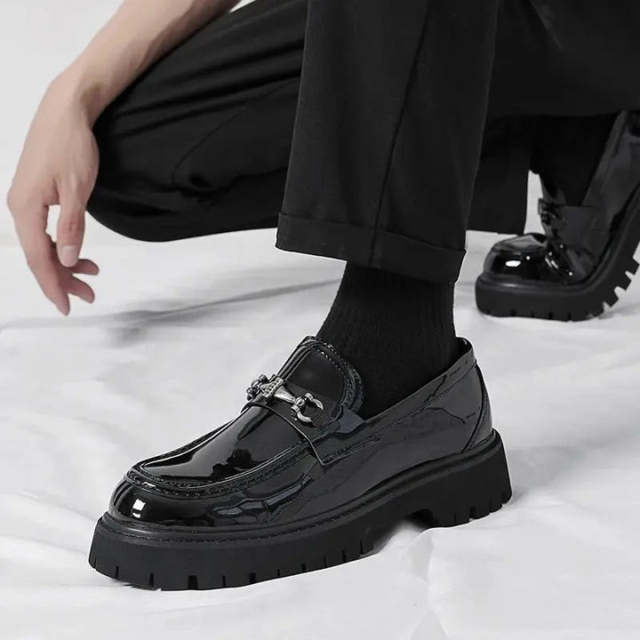 Model crouching in black patent loafers with socks, showcasing buckle detail