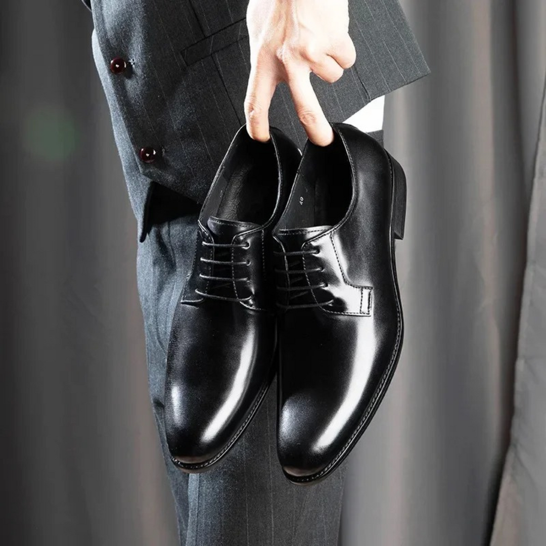 Black leather derby dress shoes with lace-up detailing held against a pinstripe suit