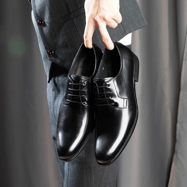 Black leather derby dress shoes with lace-up detailing held against a pinstripe suit