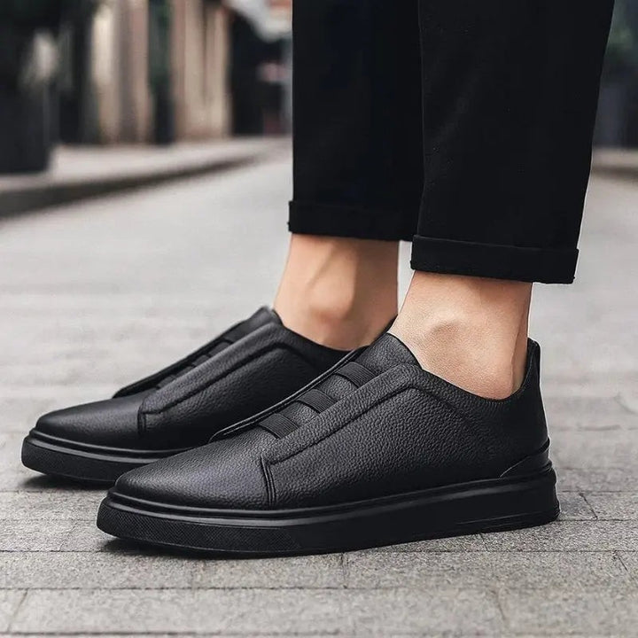 Man walking in all-black leather slip-on trainers with elastic loop laces