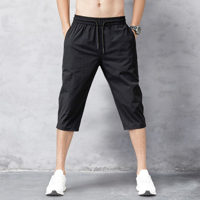 Black cropped jogger trousers with elastic drawstring waistband, side view of pockets