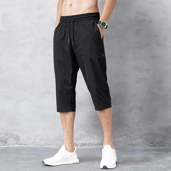 Black cropped running trousers shown from the side with tapered hem and trainers