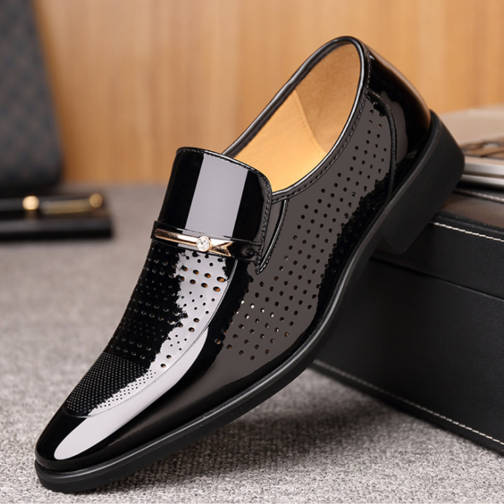 Black patent loafer featuring perforated side panel and gold buckle detail