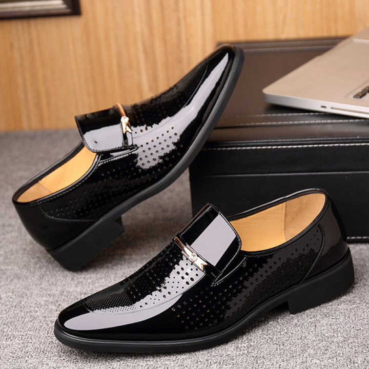 Pair of black patent leather loafers with perforated panels on wooden floor
