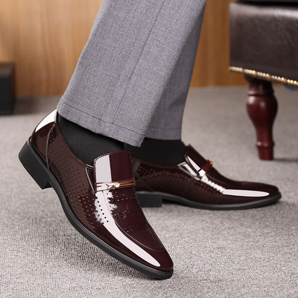 Burgundy patent loafer worn on foot with grey tailored trousers