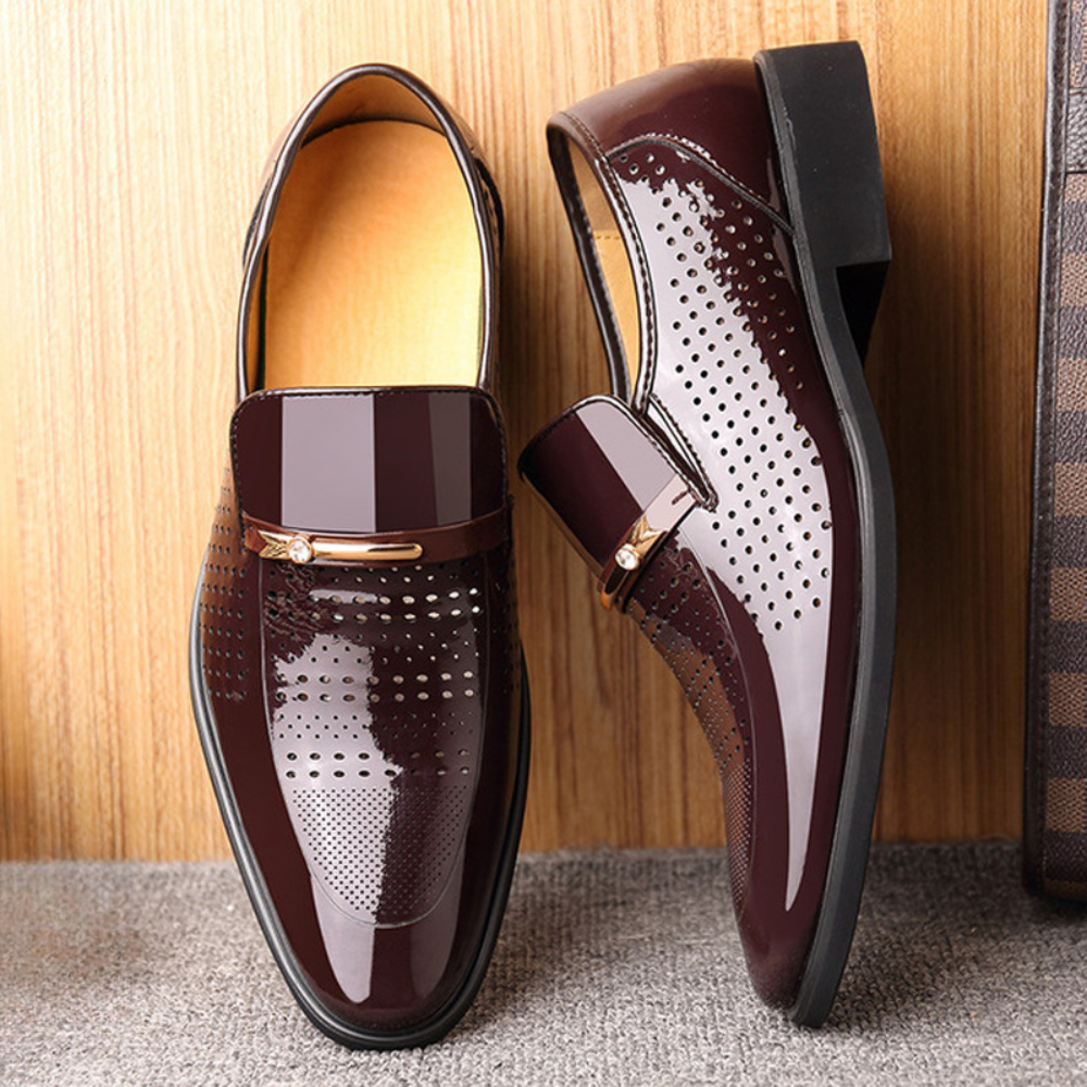 Pair of burgundy patent leather loafers with perforated panels against wood