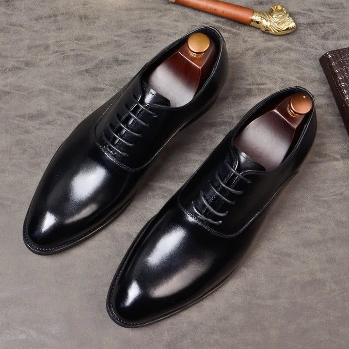 Black leather Oxford shoes with pointed toe displayed with wooden shoe trees