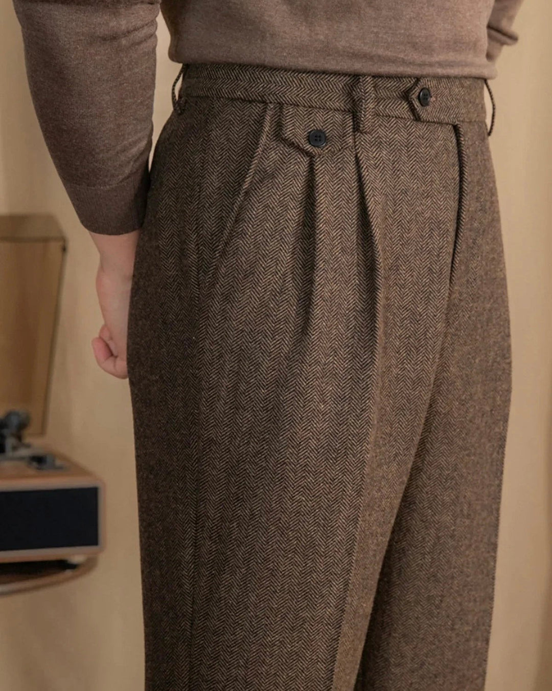 Brown herringbone wool trousers featuring high-waisted pleats and buttoned coin pocket