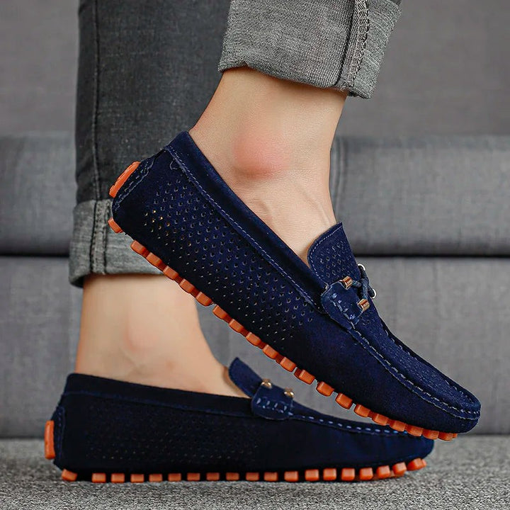 Navy perforated suede loafers worn on foot with orange studded sole