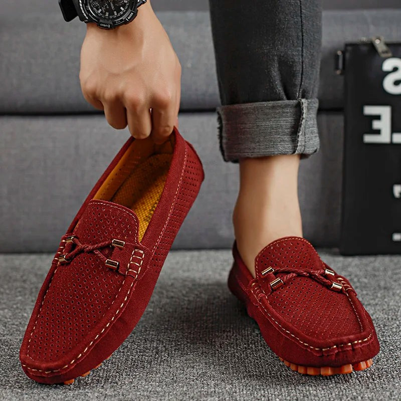 Burgundy suede perforated loafers held by hand, showing tan lining