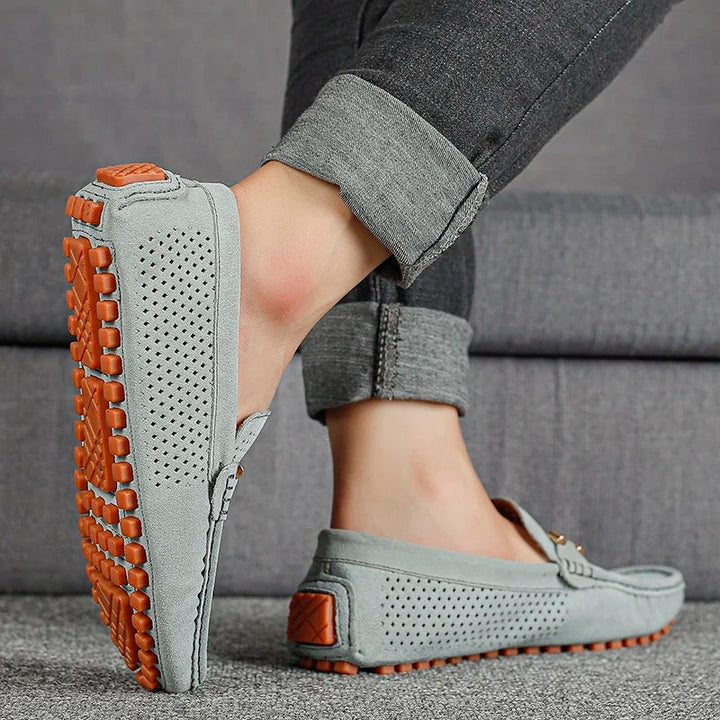 Grey suede perforated loafers worn on foot, highlighting orange grip sole
