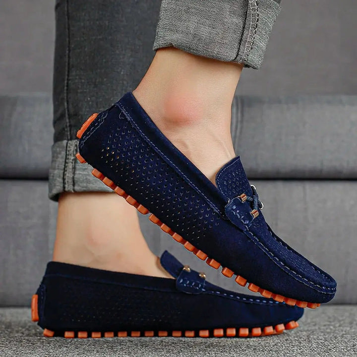 Navy perforated suede loafers worn on foot with tasselled lace trim