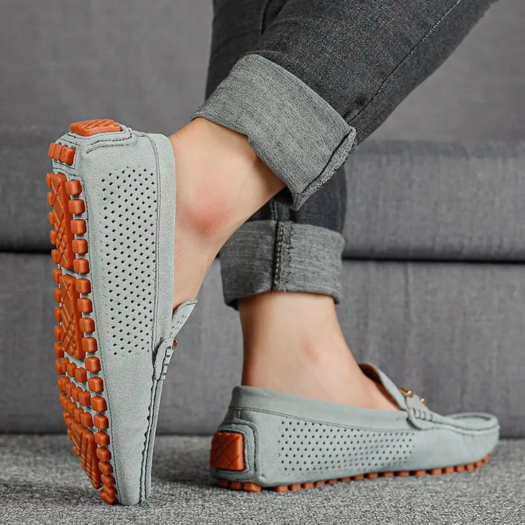 Grey suede loafers worn on foot, highlighting textured orange rubber sole