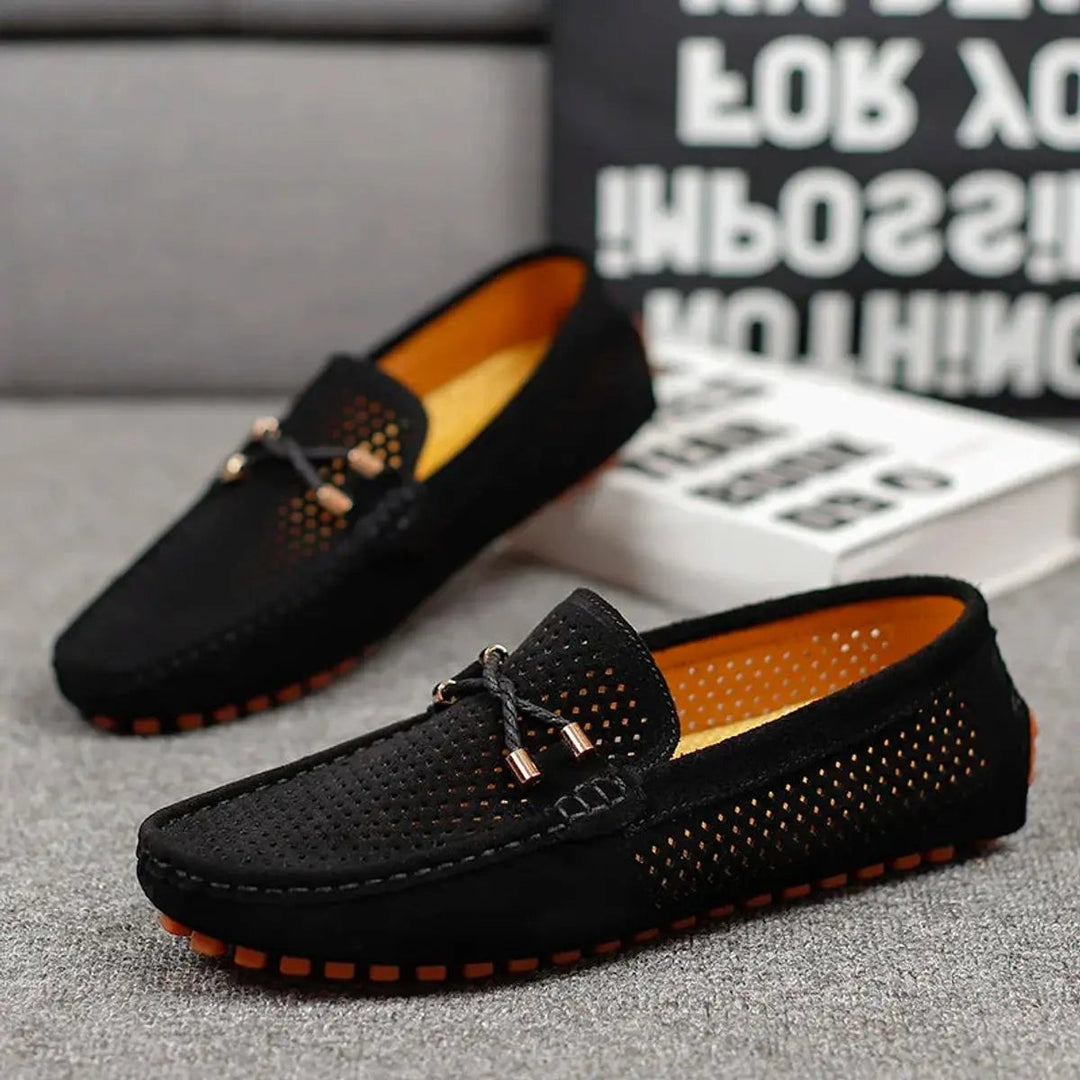 Black suede driving loafers paired together, showing orange interior lining