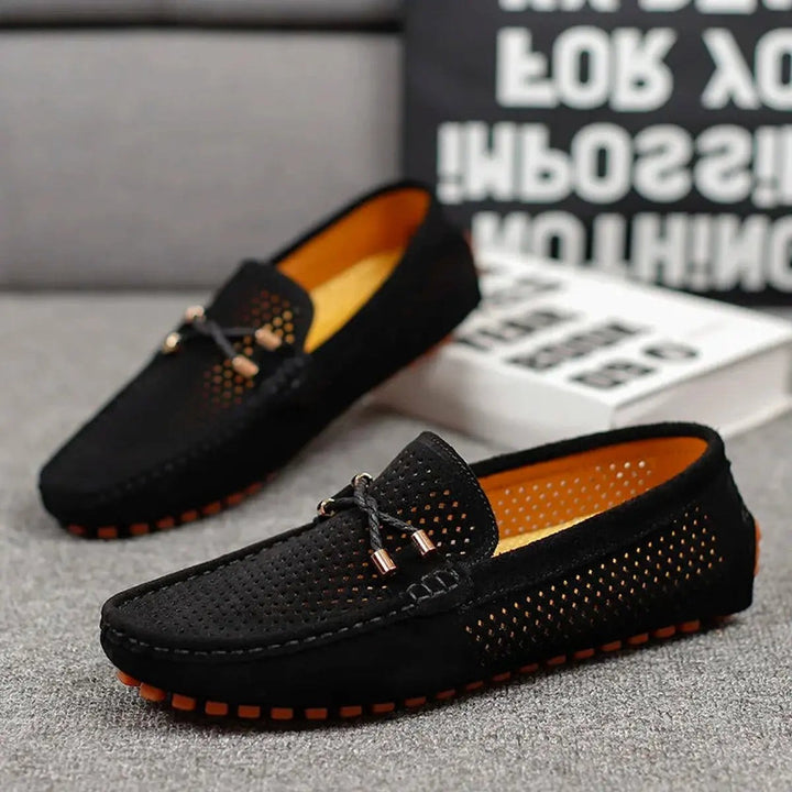 Black suede driving loafers paired together, showing orange interior lining