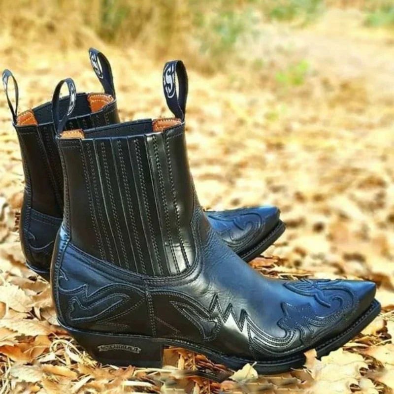 Pair of black leather cowboy boots with elasticated side panels on autumn leaves
