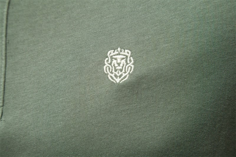 Close-up of embroidered lion crest logo on olive green polo