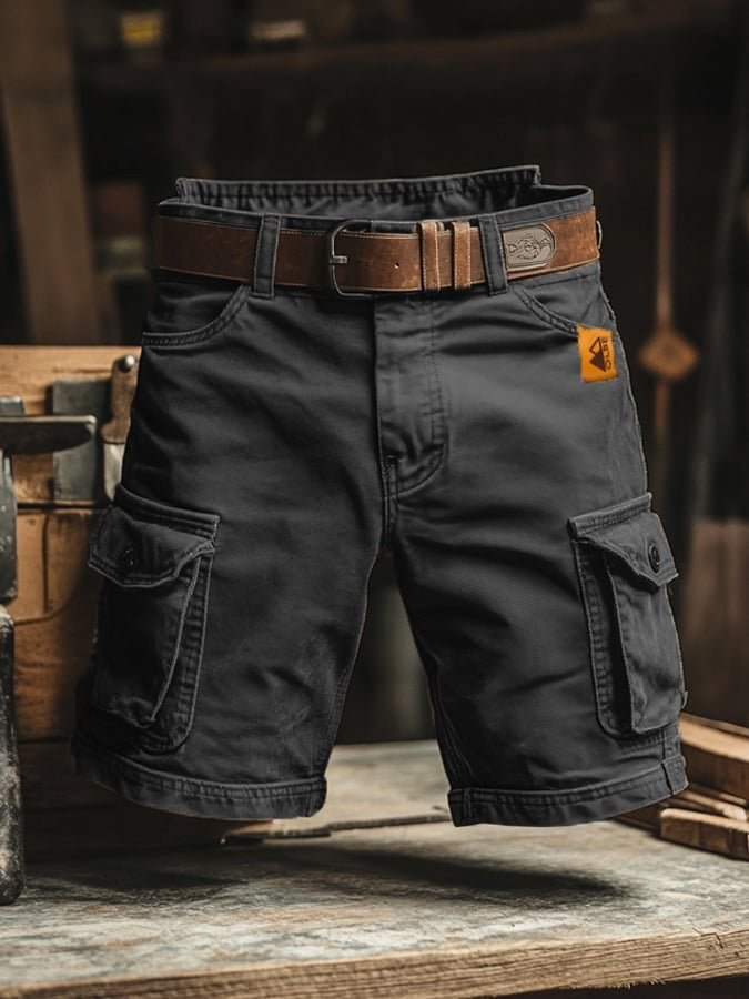 Black cargo shorts with leather belt and side pocket detailing, workshop backdrop