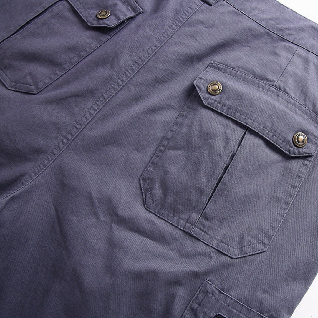 Grey cargo shorts detail showing press-stud flap pocket with brass button