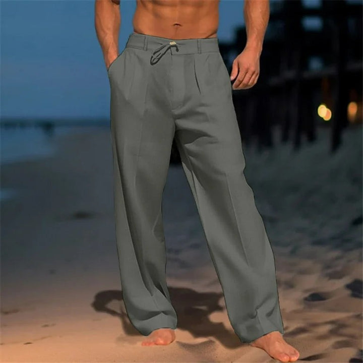 Grey wide-leg men's trousers with drawstring waist, shown against evening beach backdrop