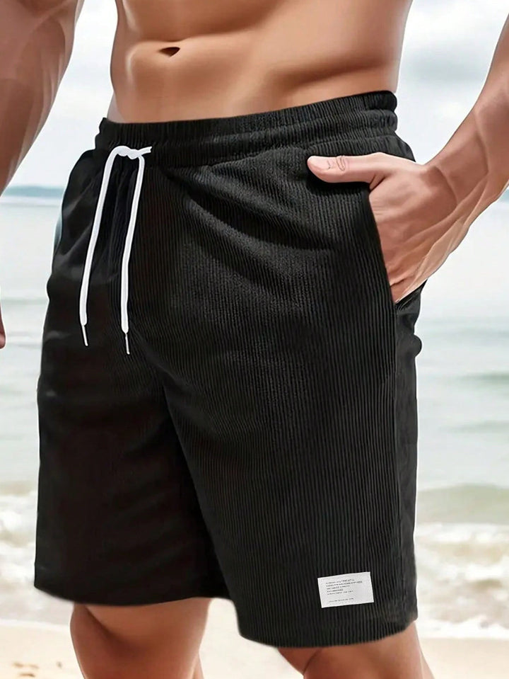 Black ribbed corduroy shorts with white drawstring, worn at beach setting