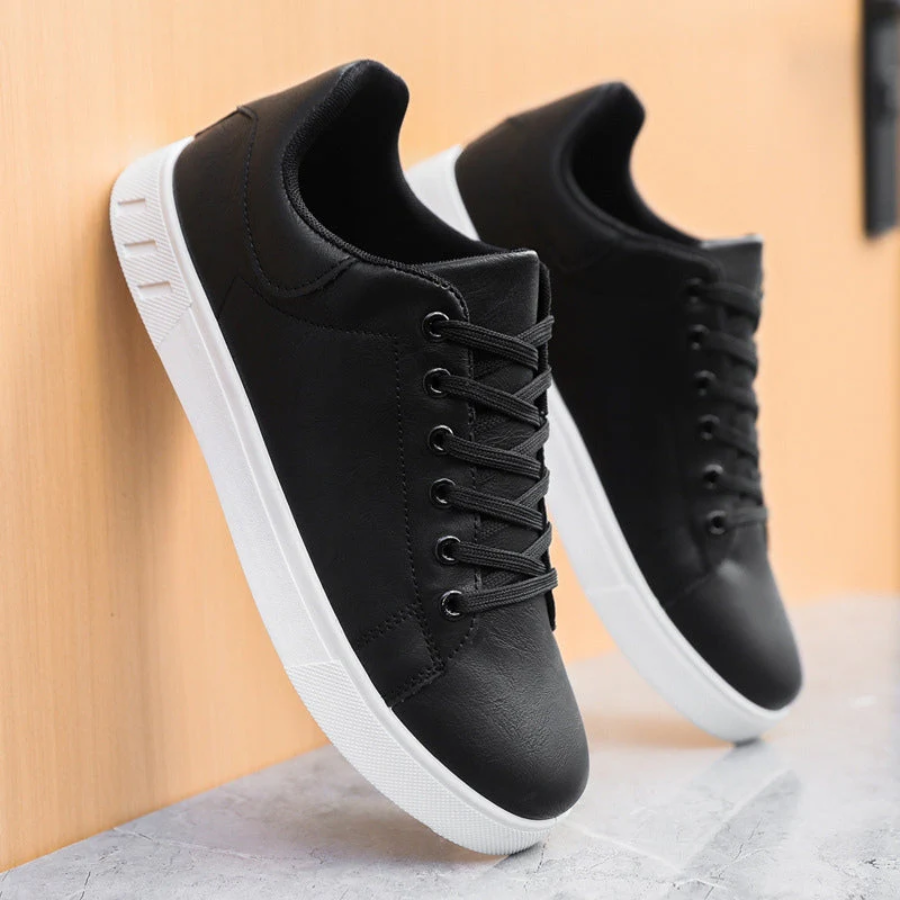Black leather trainers with white soles leaning against wooden panel