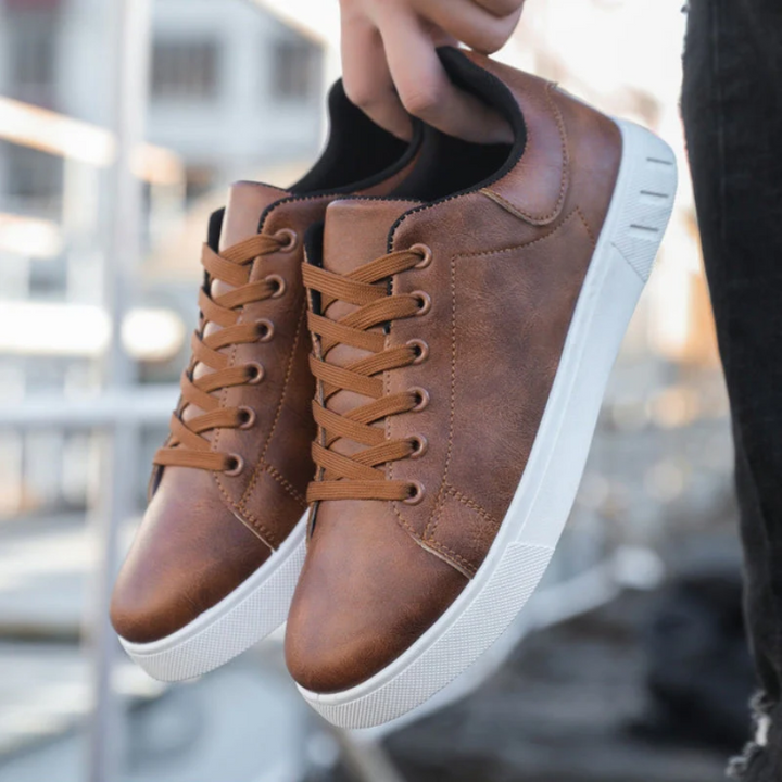 Tan leather lace-up trainers held by hand against marina backdrop