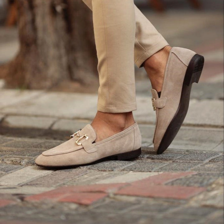 Beige suede loafers with gold-tone snaffle buckle, worn with tailored trousers