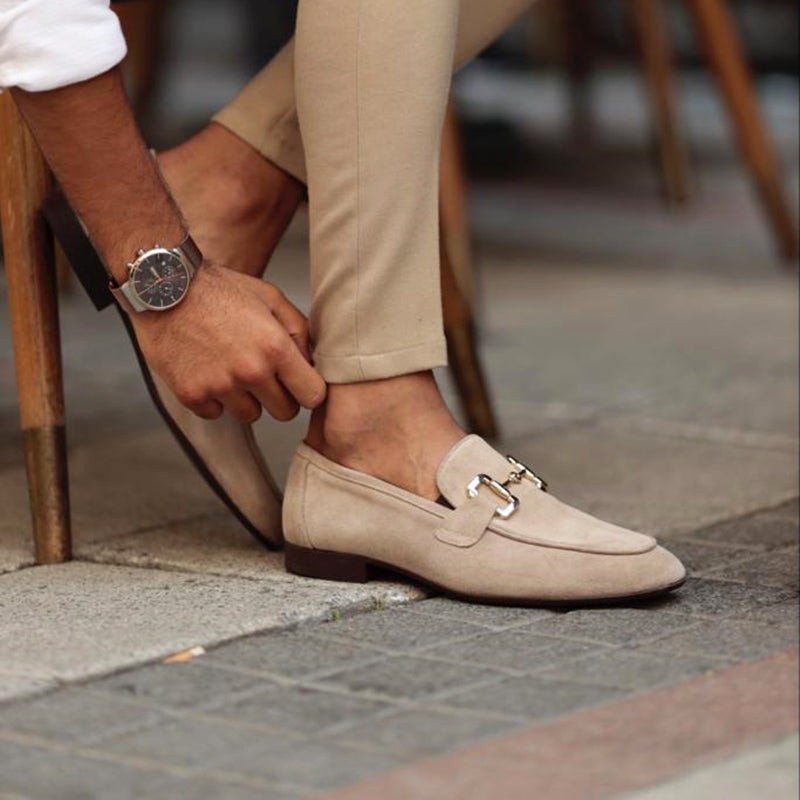 Close-up of taupe suede loafer with gold buckle detail, slipped on outdoors