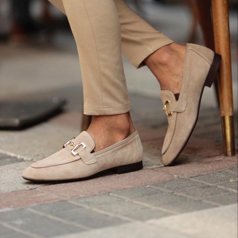 Model striding in beige suede loafers with gold horsebit hardware, cobbled street