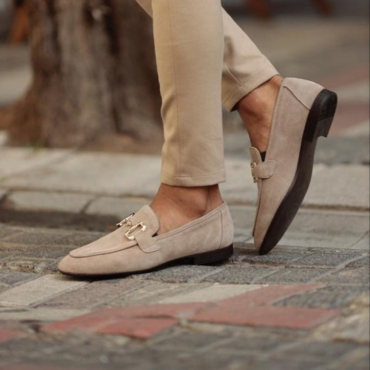 Beige suede loafers with metal snaffle detail, shown mid-stride outdoors