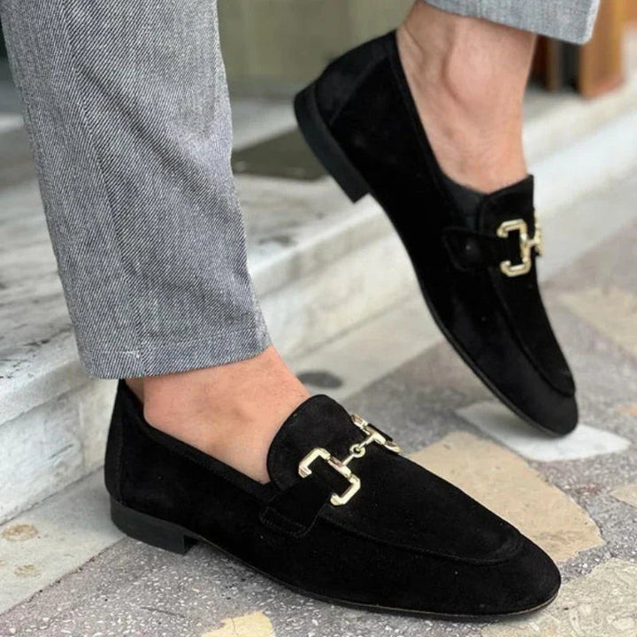 Black suede loafers with gold hardware, worn with grey tailored trousers
