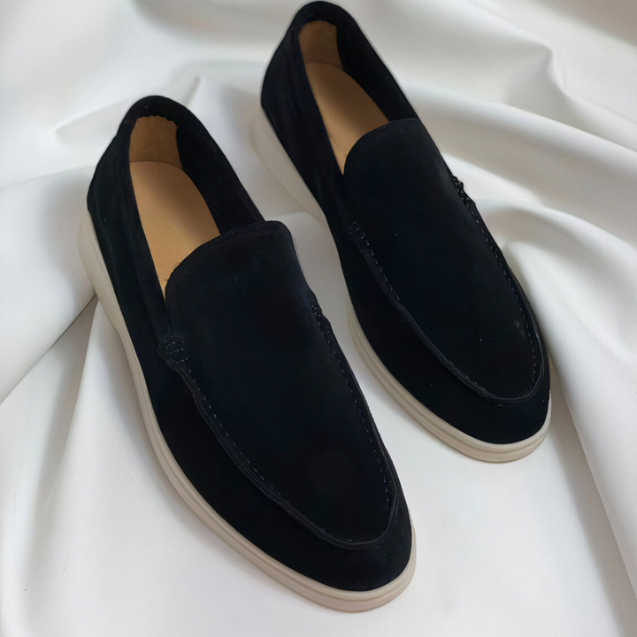 Black suede loafers with cream soles displayed on draped white fabric