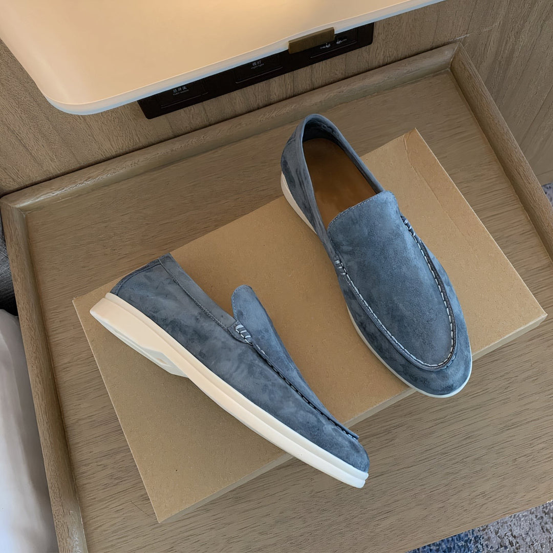 Grey suede loafers resting on wooden bedside table with white soles