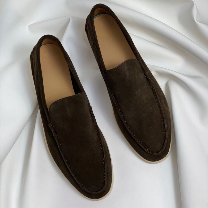 Dark brown suede loafers with white soles on white fabric backdrop