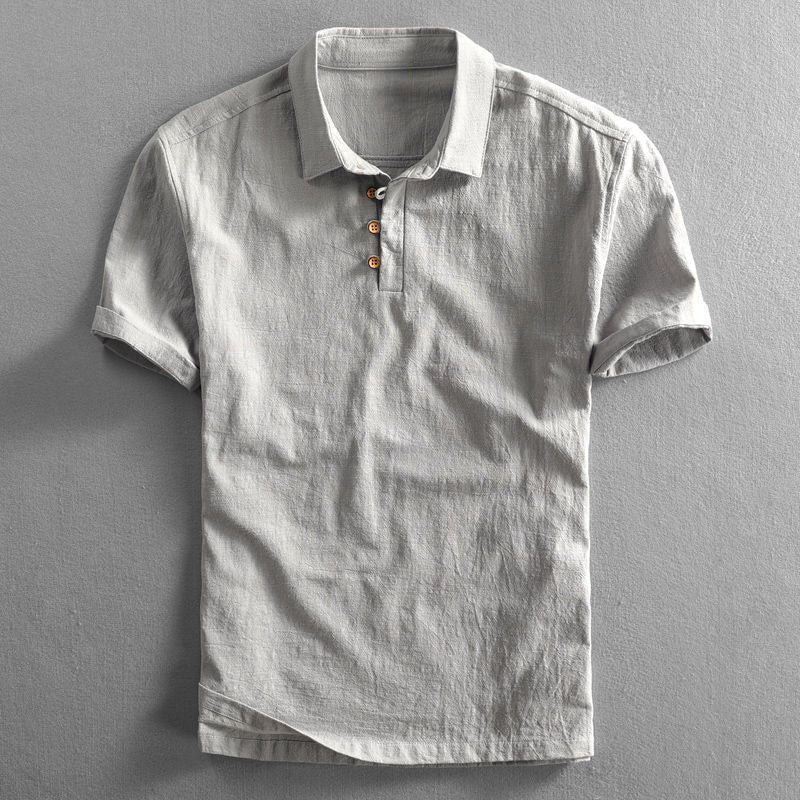 Grey linen polo shirt with wooden buttons, folded neatly against backdrop