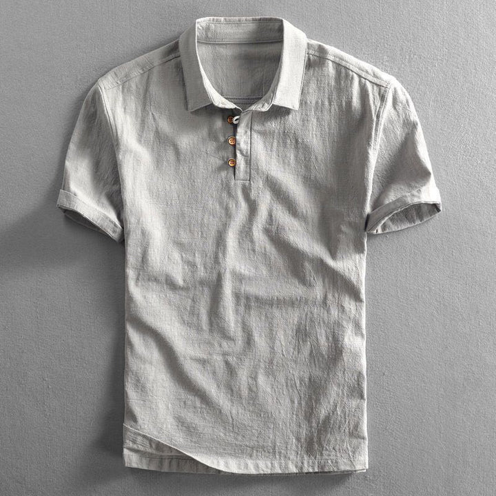 Grey linen polo shirt with wooden buttons, folded neatly against backdrop