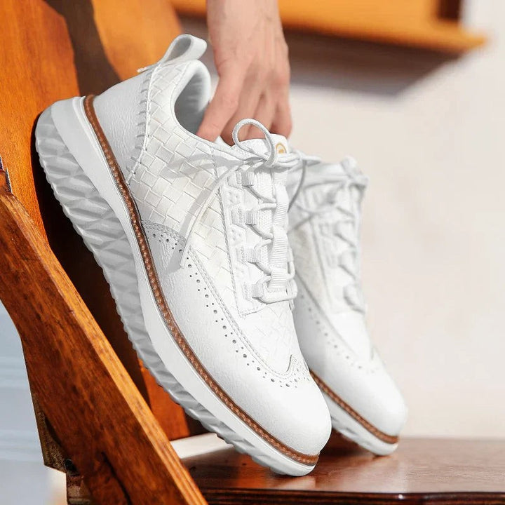 White woven leather platform trainers held by hand beside a wooden chair