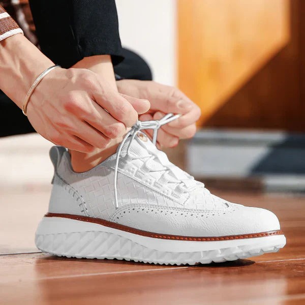 White leather trainers being laced up, showing brogue perforations and woven panel