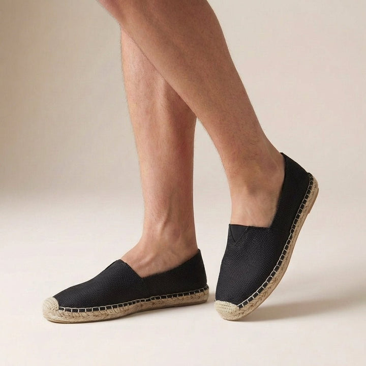 Black woven slip-on espadrilles with jute-wrapped sole, worn on feet