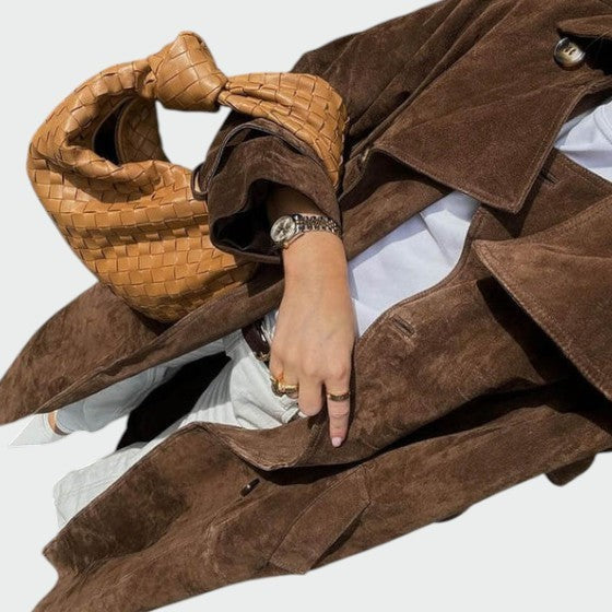 Close-up of brown suede trench coat sleeve paired with a woven tote bag