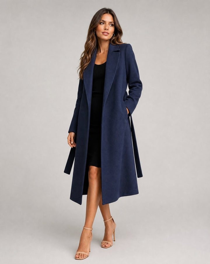 Navy belted longline coat worn open over a black midi dress with tailored lapels