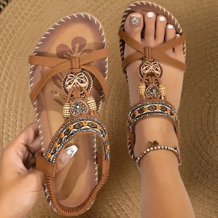 Tan flat sandals with crossover straps and beaded butterfly charm