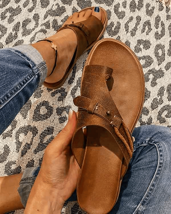 Tan toe-post flat sandal with buckle detail held above matching pair