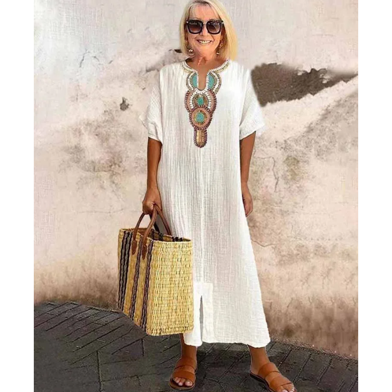 White embroidered kaftan maxi dress styled with woven straw tote bag